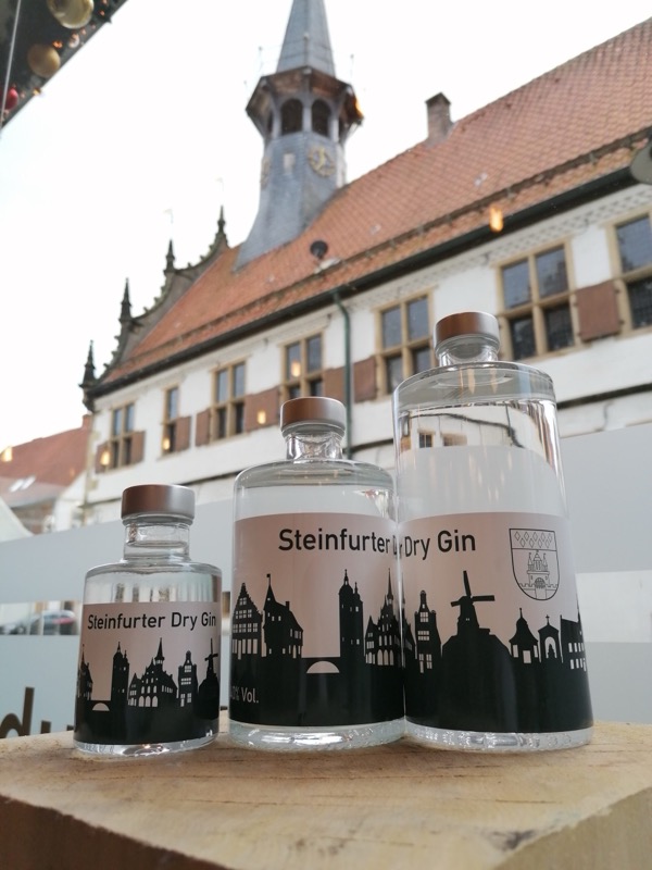 Drei Flaschen Steinfurter Dry Gin in verschiedenen Größen vor dem historischen Rathaus Steinfurt